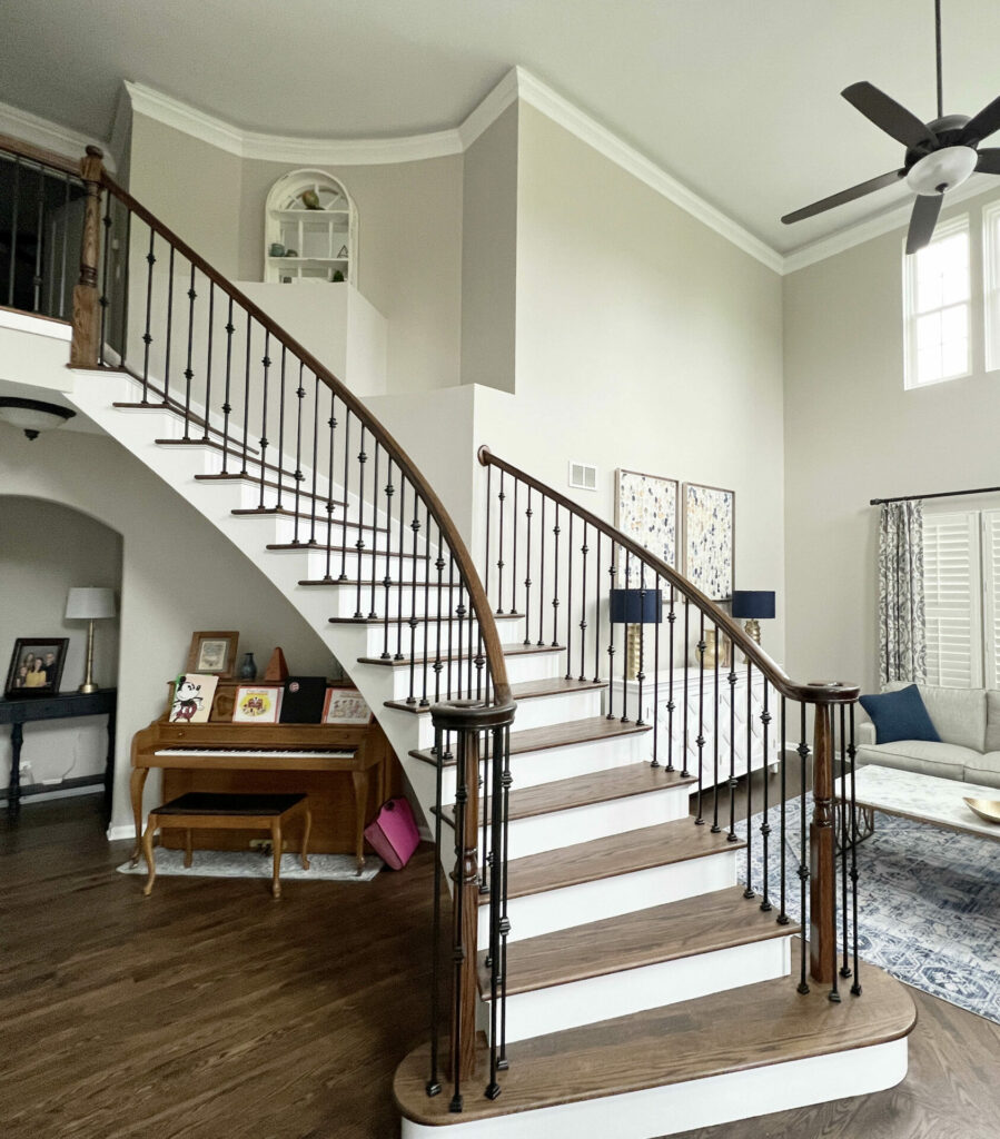 Curved wood staircase with white painted risers, iron balusters and a wooden newel post