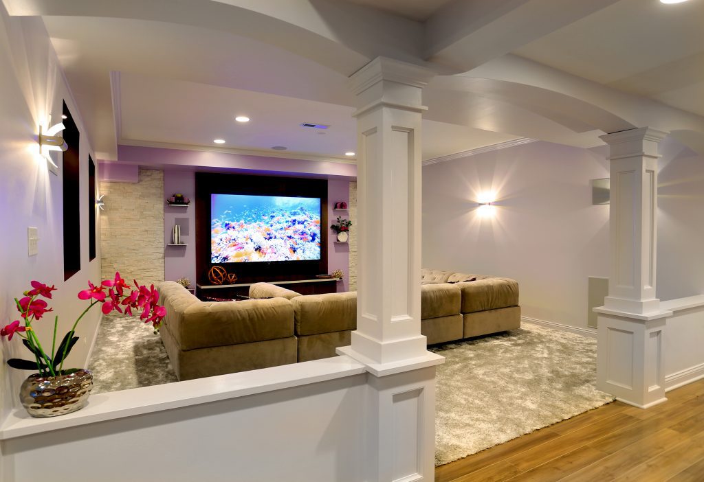 Big screen TV in basement with sectional and decorative columns