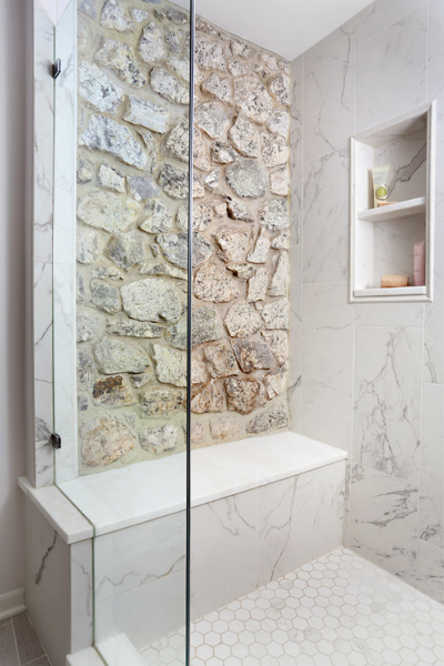 master bathroom shower with exposed stone behind bench