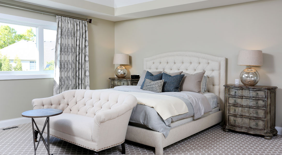 master bedroom with tray ceiling and settee at the end of the bed