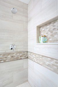 master bathroom shower with decorative tile band and matching storage niche