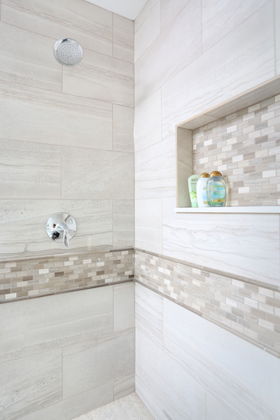 master bathroom shower with decorative tile band and matching storage niche