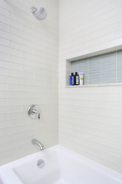 bathtub and shower combination with a colorful tile storage niche