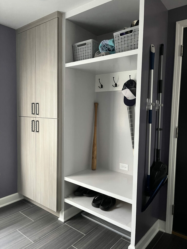 modern mudroom with closed storage doors and open cubby with hooks and shelving. Dark flooring and purple walls