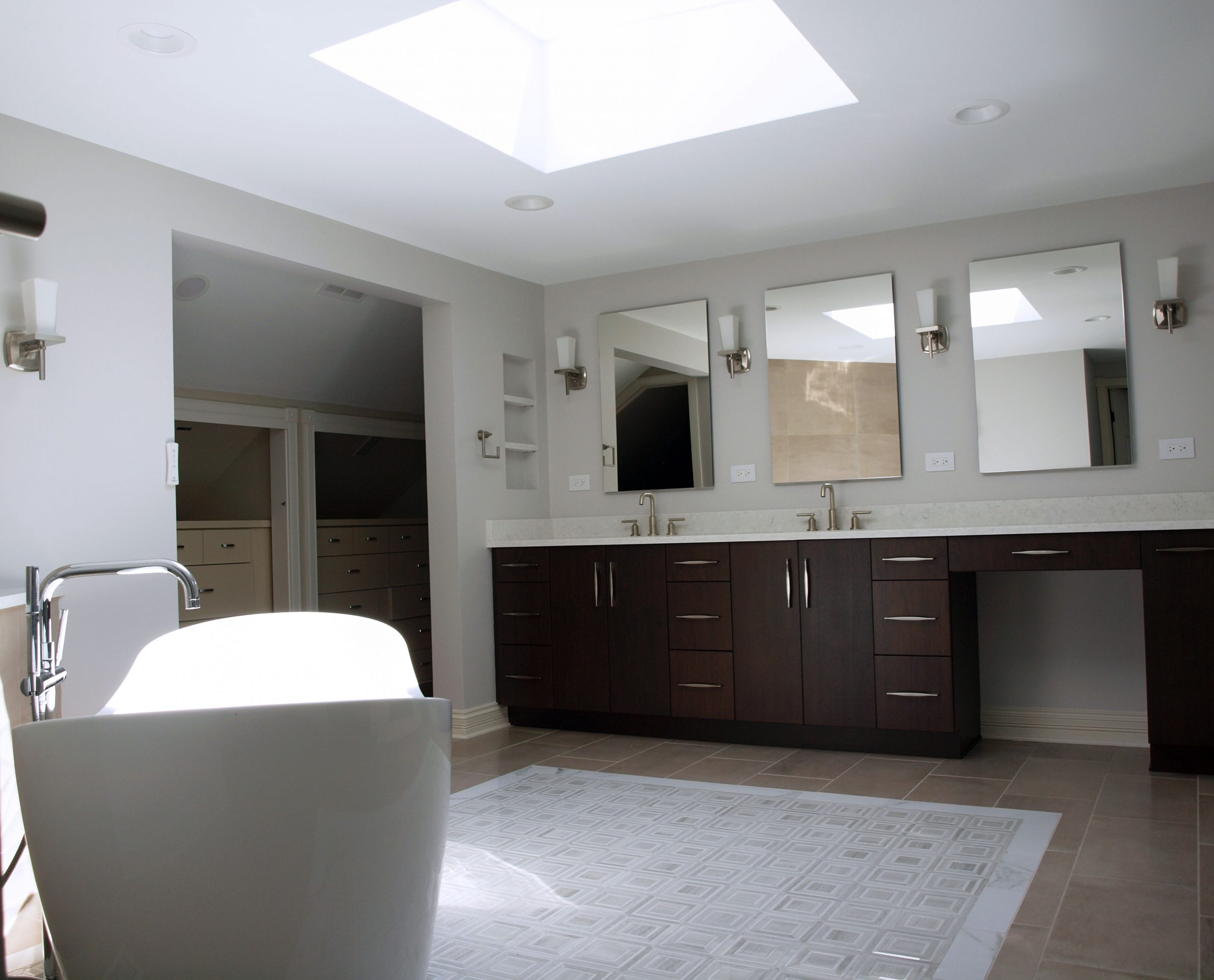 Primary bathroom with stained cabinetry, freestanding bathtub, and skylight