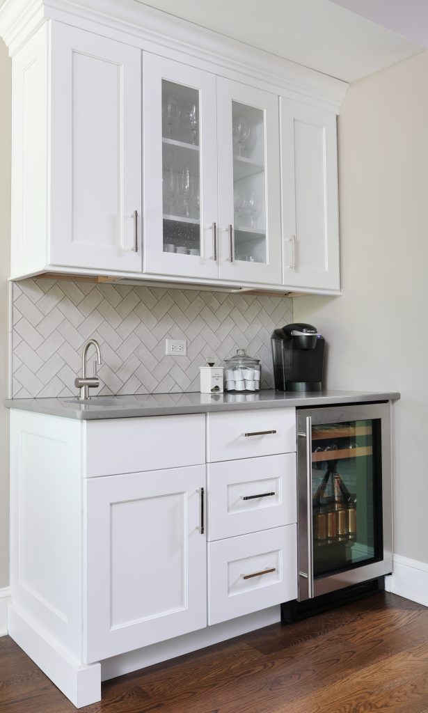 beverage center with upper cabinets, sink and herringbone backsplash