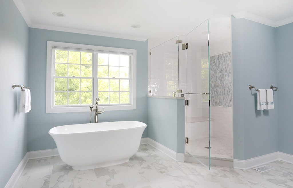 stand alone tub in front of window and shower with half wall and frameless surround