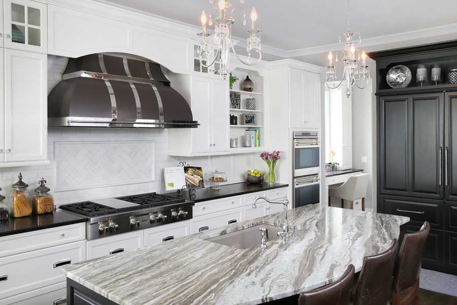 White kitchen with metal hood, black accent cabinets, and kitchen island