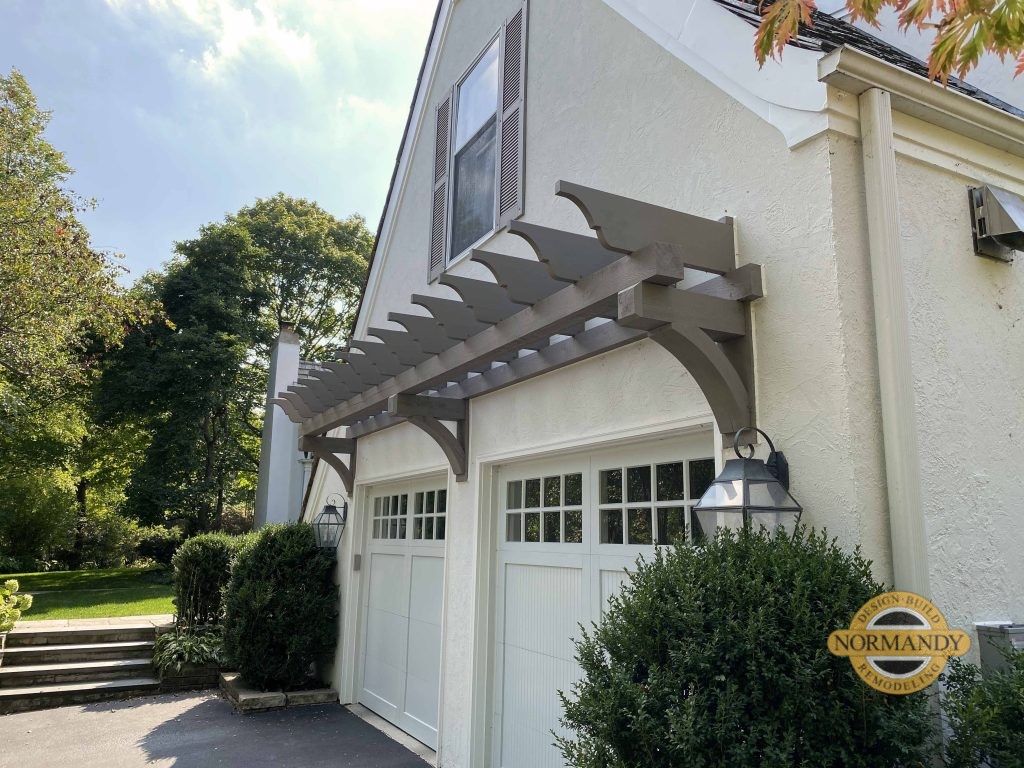 Stucco home exterior with eyebrow pergola over garage doors