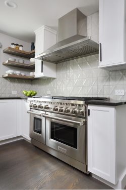 Professional grade range with stainless steel hood and open shelves and textured white backsplash tiles