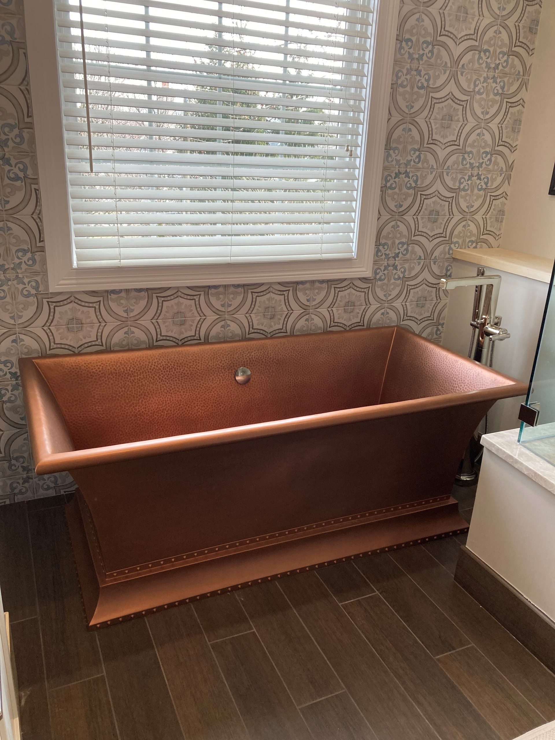 cooper bathtub with dark flooring under a window