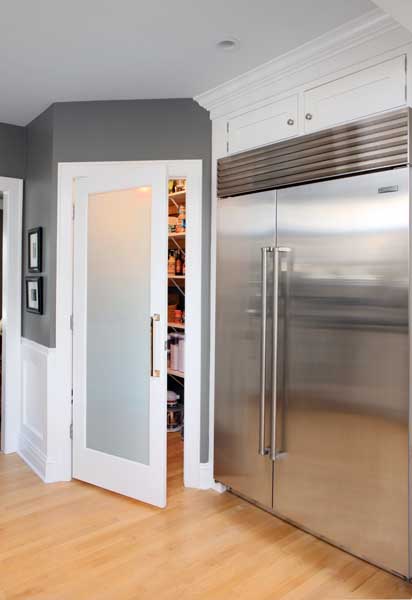 Large kitchen refrigerator next to walk-in pantry with frosted door