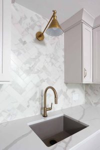 Marble-look porcelain tile backsplash to the ceiling, brass faucet, brass light fixture