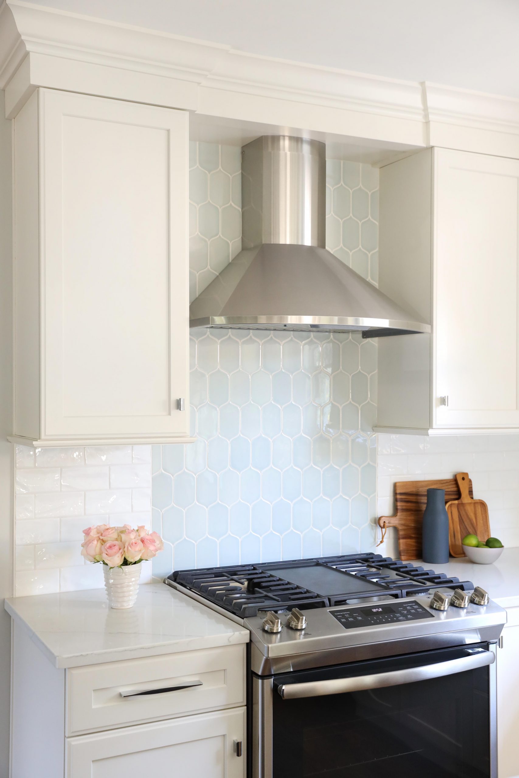 White kitchen cabinets with pale blue accents at the range and stainless steel range hood