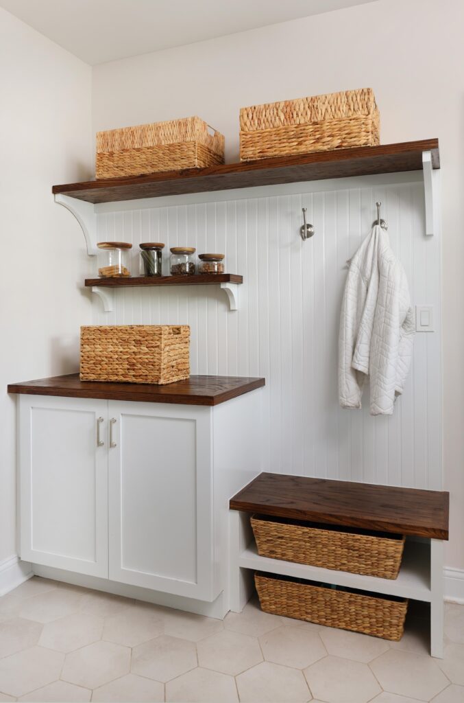 white paneled wall in mudroom with hexagon floor tile and dark wood shelving