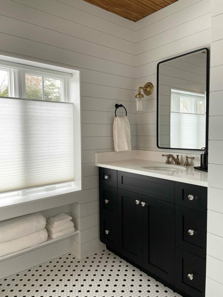 vintage bathroom with dark vanity, glass knobs, black and white mosaic floor tile and shiplap walls