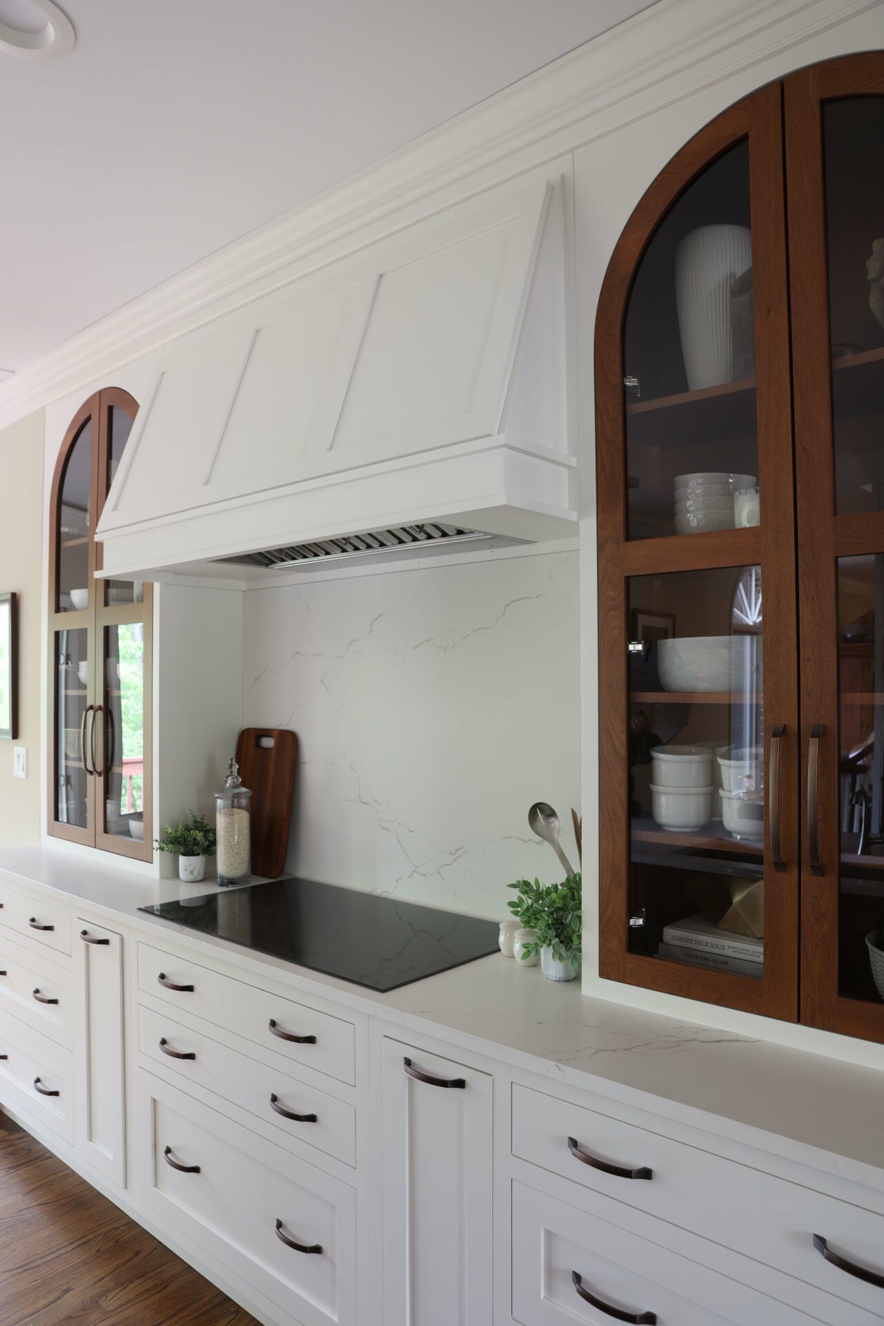Modern traditional kitchen features winter white cabinetry and contrasting arch top cherry cabinets on either side of the cooktop