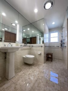 Wide shot of open concept accessible bathroom with doorless shower, floating toilet and mirrors that wrap around the room