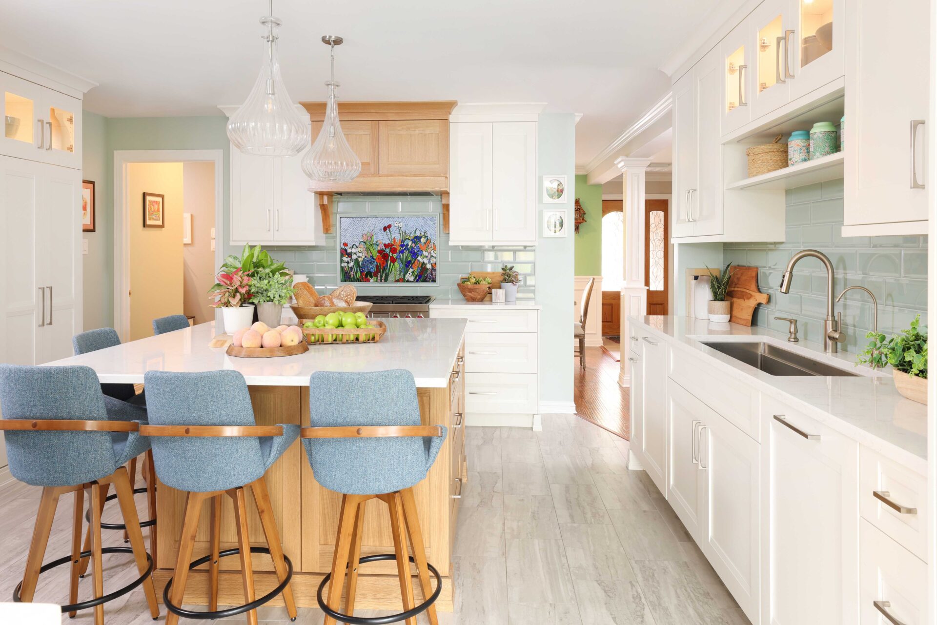 White kitchen cabinets and countertops, rift cut white oak range hood and kitchen island, color mosaic backsplash light blue fabric high-backed bar stools, kitchen sink