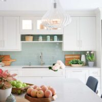 White kitchen cabinets with light green tile subway tile backsplash behind kitchen sink