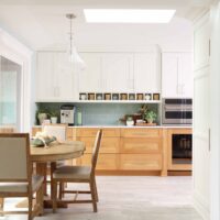 On the left, sliding patio door, and kitchen table with chairs. Coffee bar with upper white cabinets, rift cut white oak lower cabinets, coffee mugs in shelf nooks, light green tile backsplash, subway tile. Microwave and beverage/bar fridge refrigerator