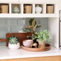 Coffee mugs and ceramic bowls in white shelf nooks. Light green subway tile backsplash.