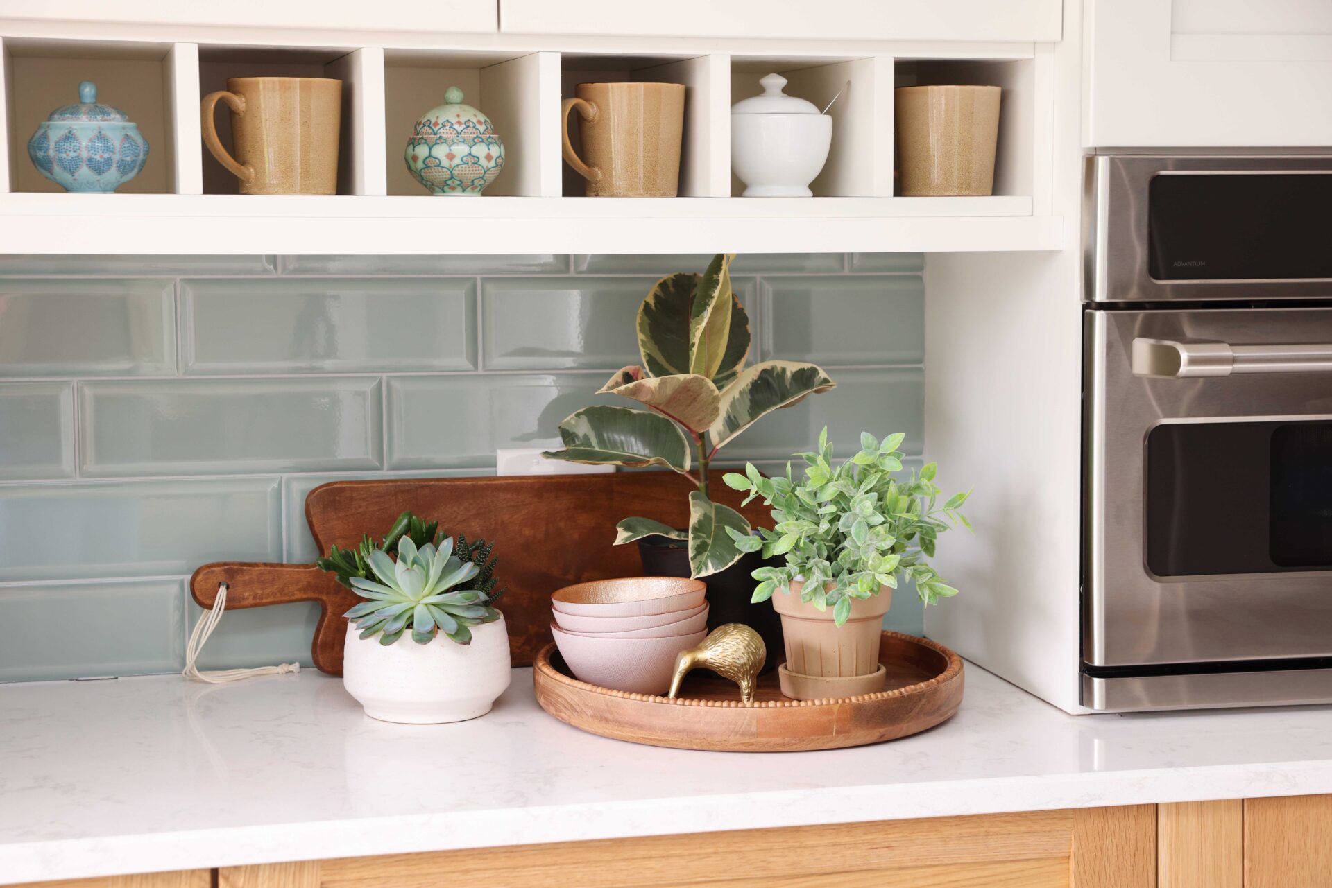 Coffee mugs and ceramic bowls in white shelf nooks. Light green subway tile backsplash.