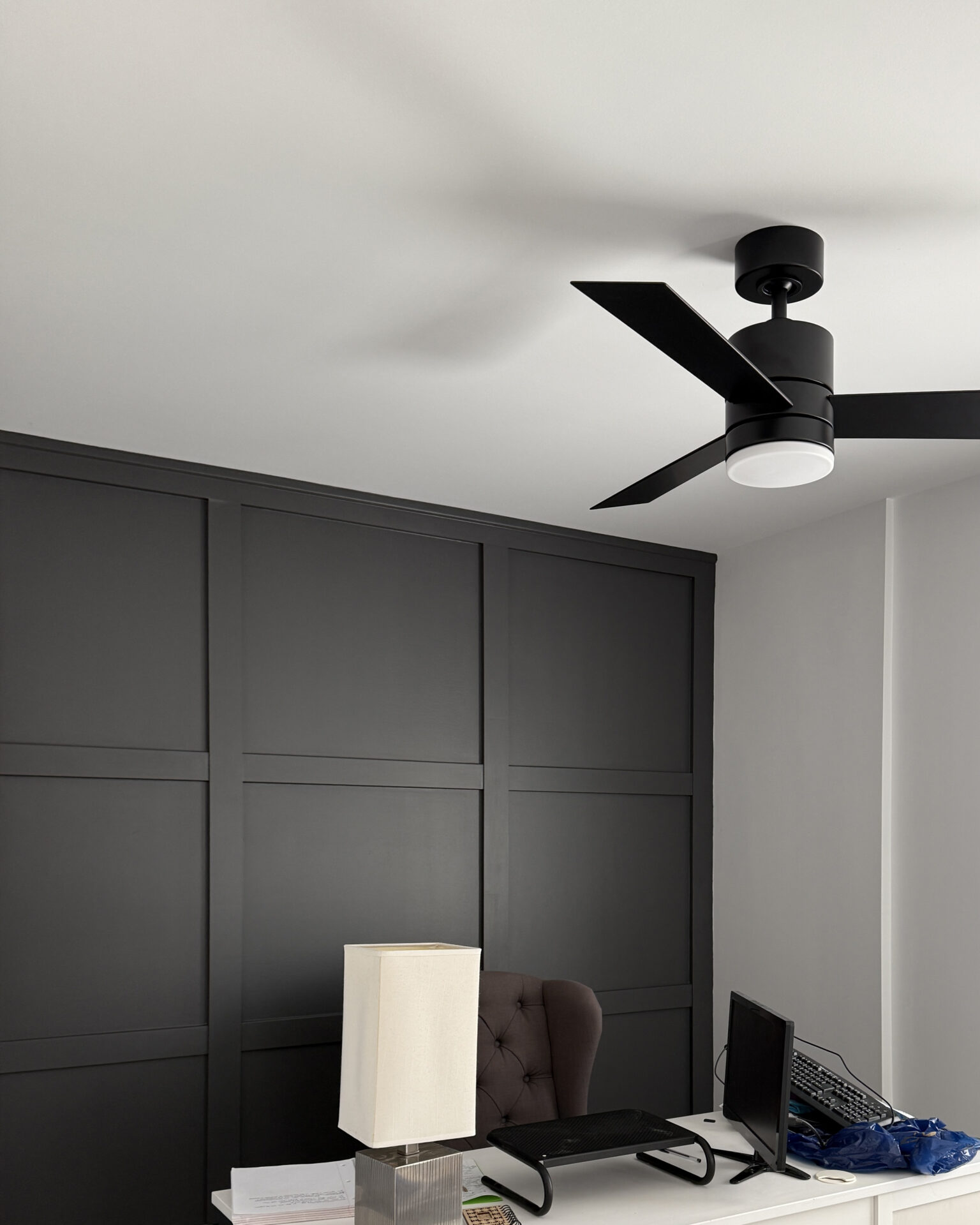 Home office in home addition with black matte wainscoting wall and matte black ceiling fan