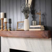 White stone fireplace face, wood mantle, dark painted wainscot paneling beadboard