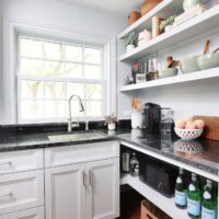 White kitchen pantry with sink, polished nickel faucet and black countertops