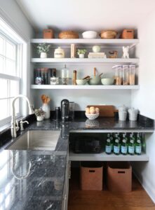 White kitchen pantry with sink, polished nickel faucet and black countertops, window above sink
