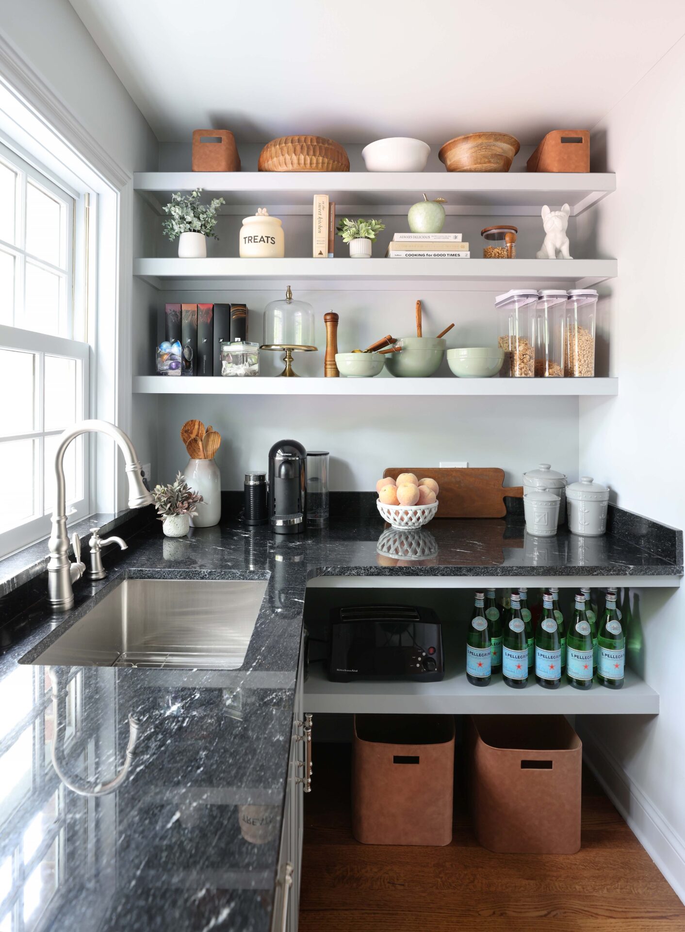 White kitchen walk-in pantry with sink, polished nickel faucet and black countertops, window above sink