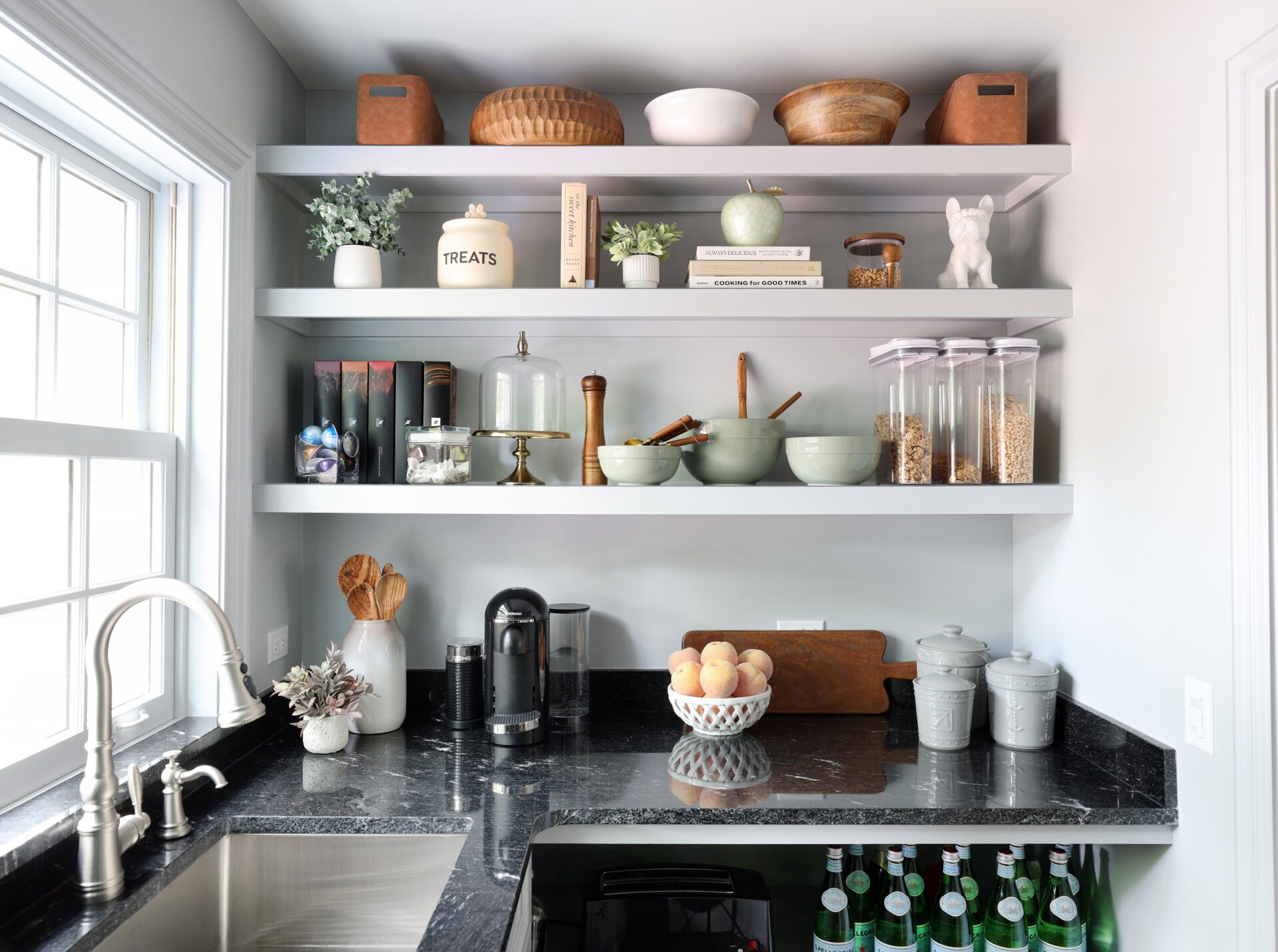 White kitchen pantry with sink, polished nickel faucet and black countertops, window above sink