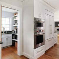Double stainless steel ovens, white paneled refrigerator, walk-in pantry with sink