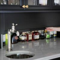 Home bar with black cabinetry, hidden appliance garage storage for liquor with door that slides up and down. Circular bar sink