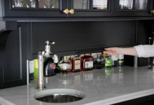 Home bar with black cabinetry, hidden appliance garage storage for liquor with door that slides up and down. Circular bar sink