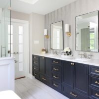 Gray herringbone textured tile vanity wall, polished nickel faucets, black rimmed mirrors, gold sconces, white quartzite counters, white tile floor