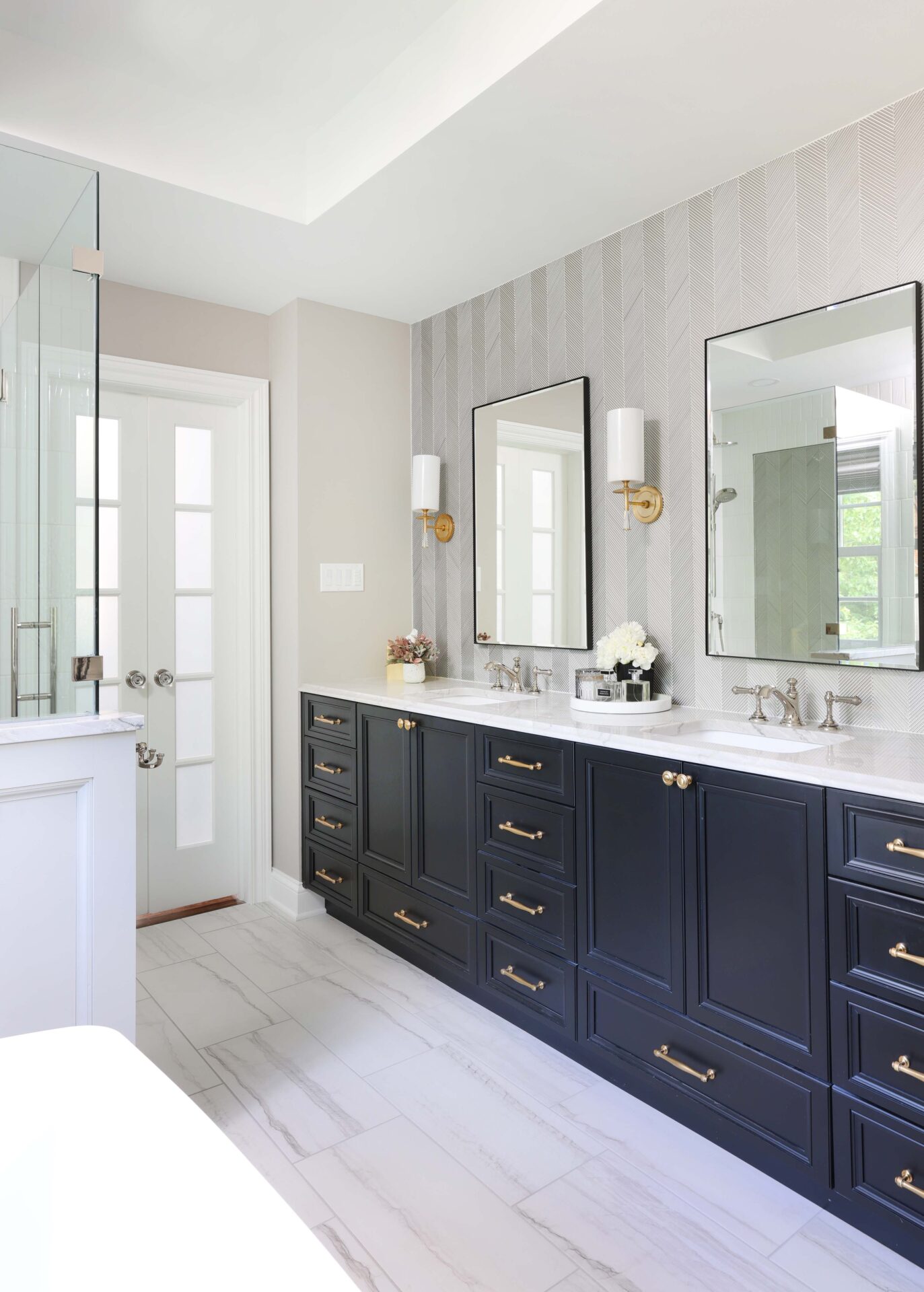 Gray herringbone textured tile vanity wall, polished nickel faucets, black rimmed mirrors, gold sconces, white quartzite counters, white tile floor