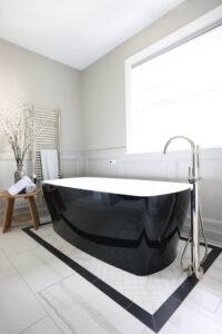 Freestanding tub with black exterior, white interior, polished nickel floor mounted faucet, towel warmer, white and black floor tile