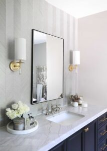 Gray glass herringbone vanity wall, textured tile, gold sconces, black vanity, black rimmed mirror, honey bronze hardware