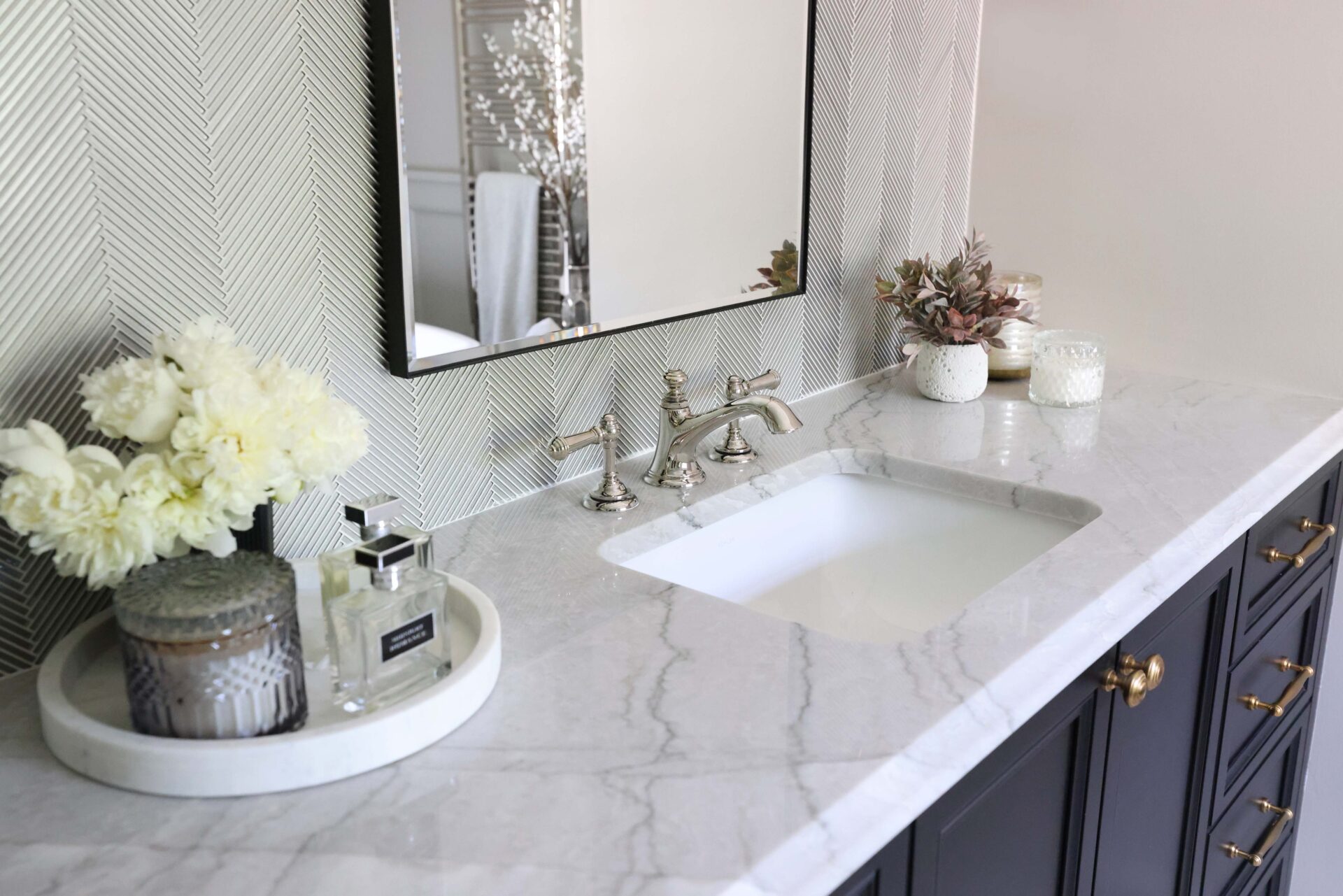 Polished nickel faucet, black rimmed mirror white quartzite countertops thick edge. Honey bronze knobs, silver textured tile vanity wall