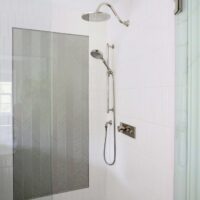 Shower accent wall of silver textured tile, surrounding white shower tile, polished nickel rain shower head and handheld shower head on slide bar