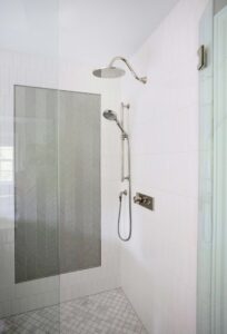 Shower accent wall of silver textured tile, surrounding white shower tile, polished nickel rain shower head and handheld shower head on slide bar