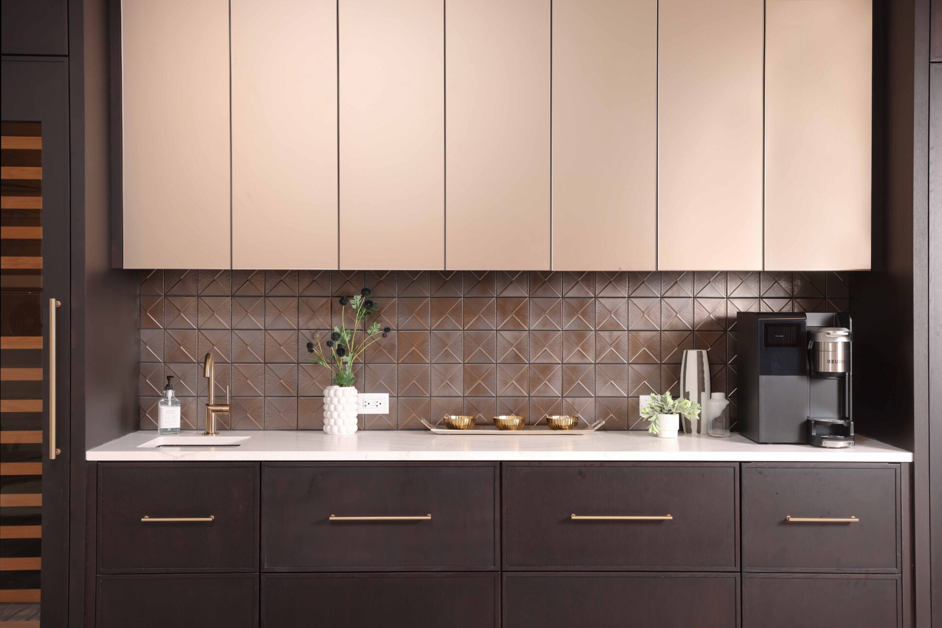The modern beverage center features rift cut white oak cabinetry, ceramic tile backsplash, quartz countertops, wine fridge, integrated refrigerator drawers, brushed brass elements, and fireclay basin.
