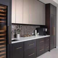 The modern beverage center features rift cut white oak cabinetry, ceramic tile backsplash, quartz countertops, wine fridge, integrated refrigerator drawers, brushed brass elements, and fireclay basin.