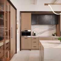 The curated modern kitchen features textured melamine cabinetry; a suite of integrated appliances including steam oven, coffee machine and induction cooktop; blackened steel range hood with brass detailing; manmade quartz waterfall island, backsplash and countertops that mimic the look of marble; loop lighting in the wall sconces and above the island.