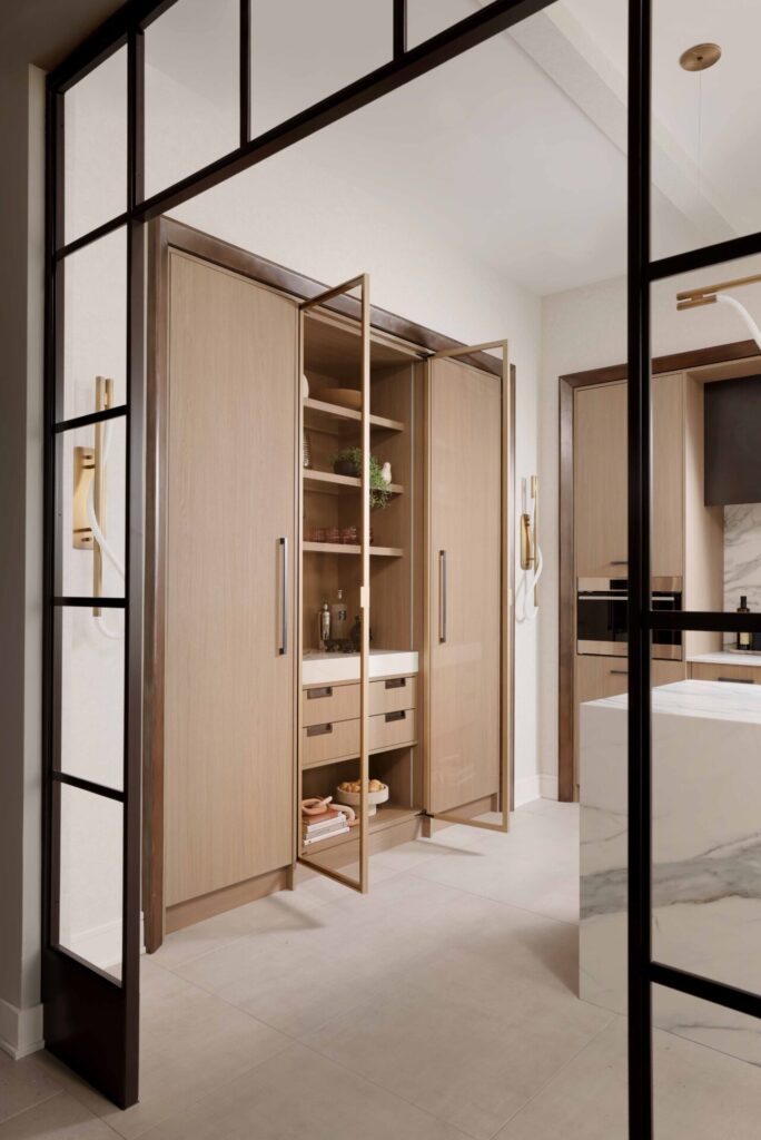 The curated modern kitchen features an integrated bar area entertainment hub with custom textured melamine cabinetry, gunmetal cabinet hardware, glass shelving, quartz counter and concealed column refrigerator and freezer. Metal trim surrounds each zone of cabinets.