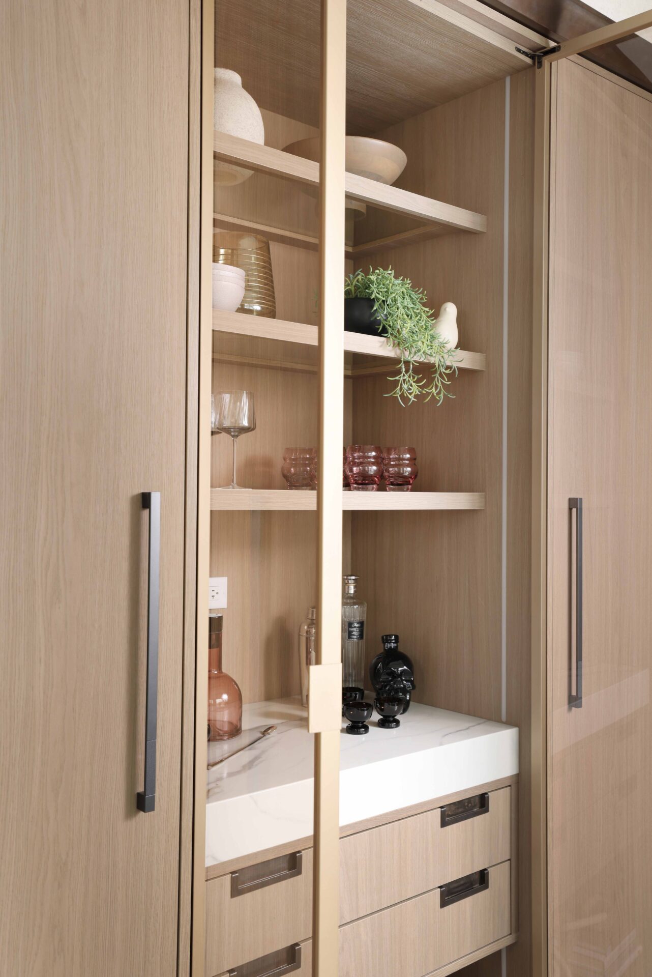 The curated modern kitchen features an integrated bar area entertainment hub with custom textured melamine cabinetry, gunmetal cabinet hardware, glass shelving, quartz counter and concealed column refrigerator and freezer.