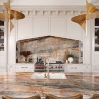 The elevated new traditional kitchen features painted cabinets throughout, color inspired by veining in backsplash and counters. Range area has recessed spice niches; flanking cabinets feature walnut interiors, ornamentation, glass shelves, accent lighting. Full height quartzite backsplash with rose and caramel veining. 48-inch range with Tudor style arched hood. Brushed bronze pot filler. Cherry stained island, thick quartzite counter with double ogee edge, furniture style legs and ample seating; sink with faucet in brushed bronze. Luxe gold pendant lights.