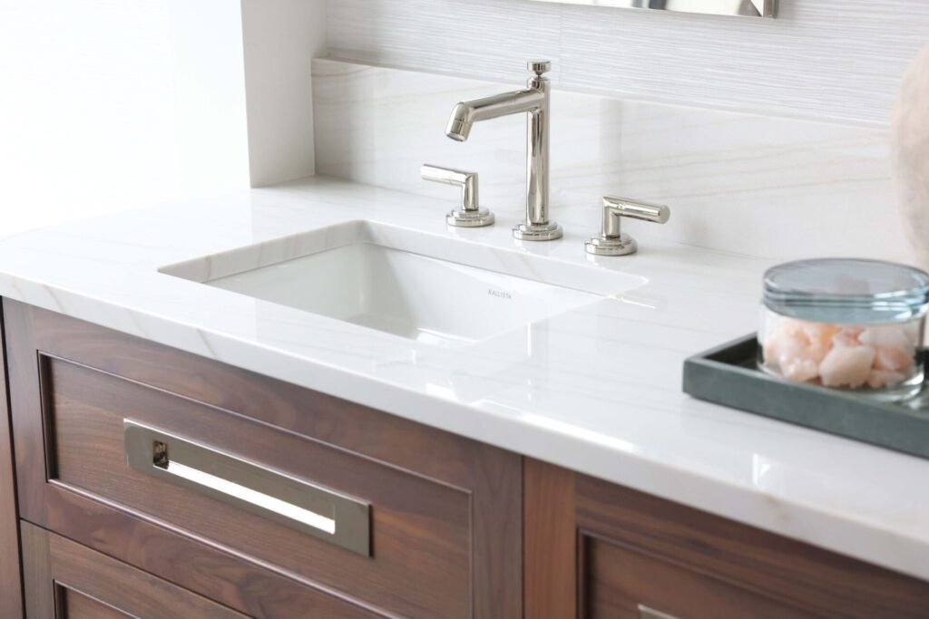 The modern classic primary bath features walnut console vanity topped with quartzite countertop and paired with a textured wallpaper backsplash.